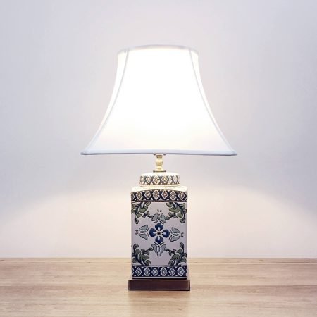 A square ceramic table lamp with a white base with green & blue floral designs and a metallic base