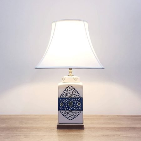 A square ceramic table lamp with a white base with green & blue floral motifs and a metallic base