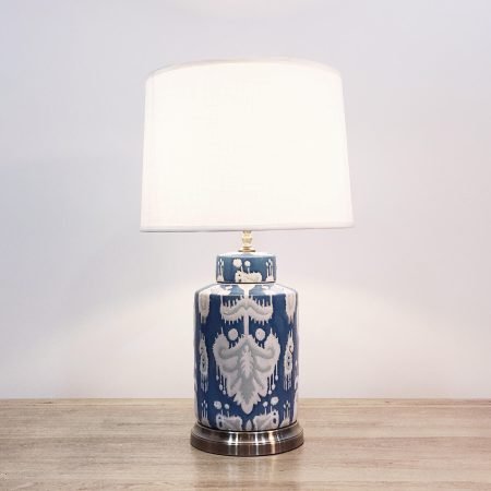 A round ceramic table lamp with a blue base and “ikat” design and a metallic base.