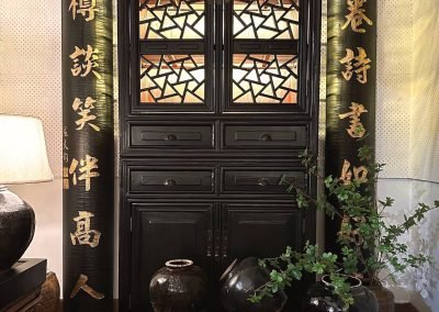 A tall black lacquered chinese antique cabinet with cracked ice lattice pattern, flanked by a pair of calligraphy couplets